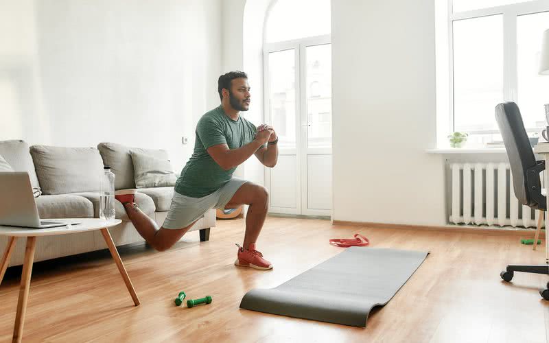 Na foto, praticante realiza o movimento "afundo" com apoio no sofá - iStock